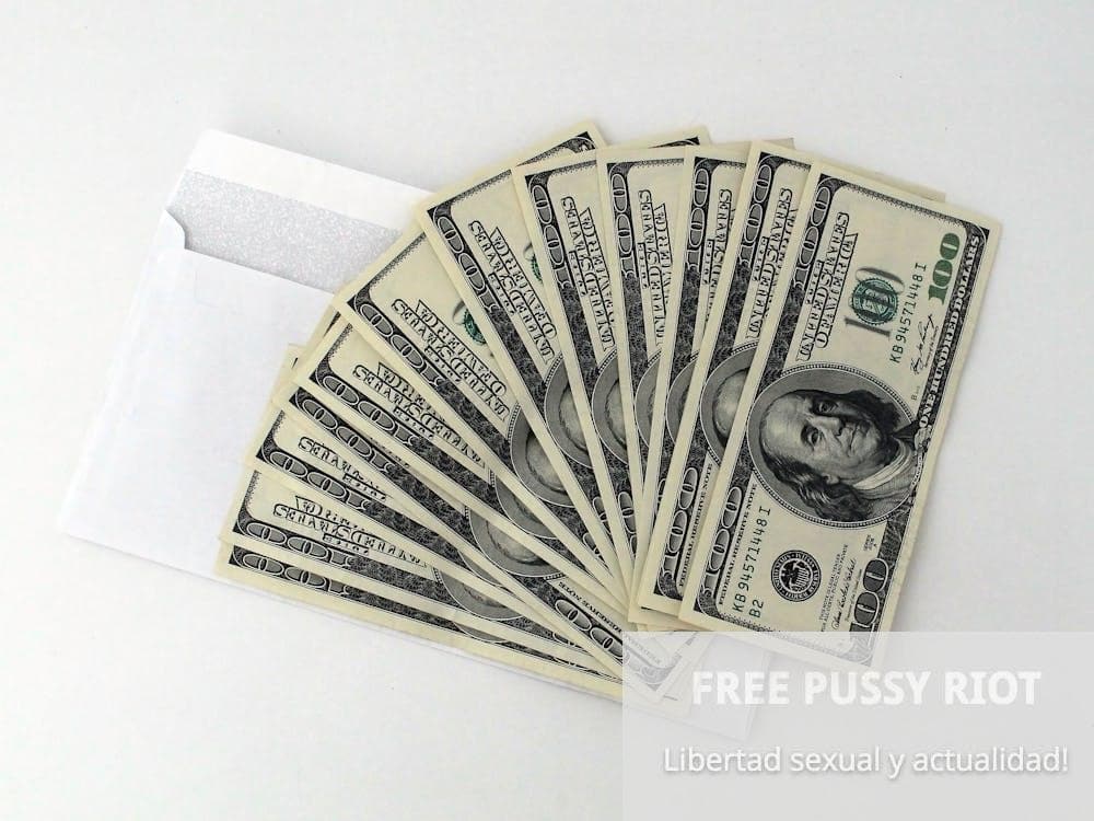Fan of US $100 bills partially out of a white envelope on a white background.